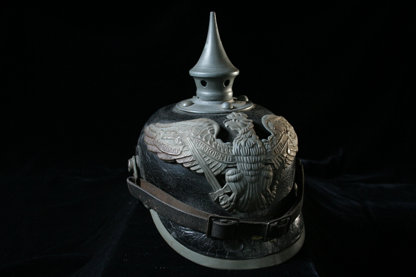 Black helmet with silver spike on top, featuring silver open winged bird detail and a leather strap and buckle across the front.  