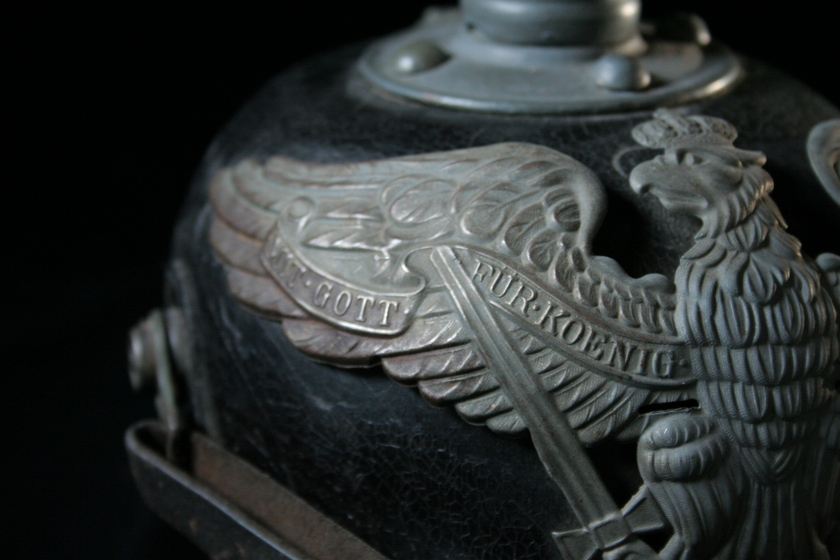Close up view of left wing of silver bird detail on black helmet, showing German text. 