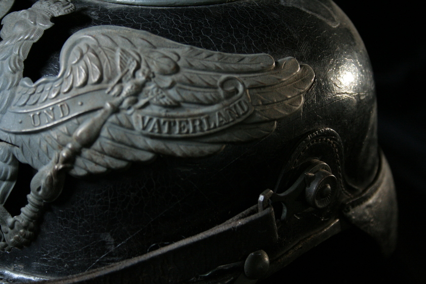 Close up view of right wing of silver bird detail on black helmet, showing German text. 