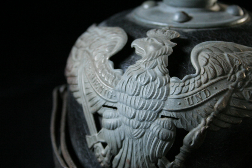 Close up view of centre of silver bird detail on black helmet, showing German text. 