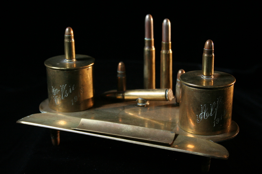 Brass item made from a flat base and attached bullets and casings, with engraved text on the casings. 
