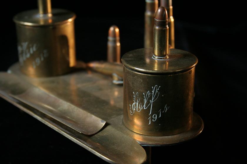 Brass item made from a flat base and attached bullets and casings, with engraved text on the casings. 