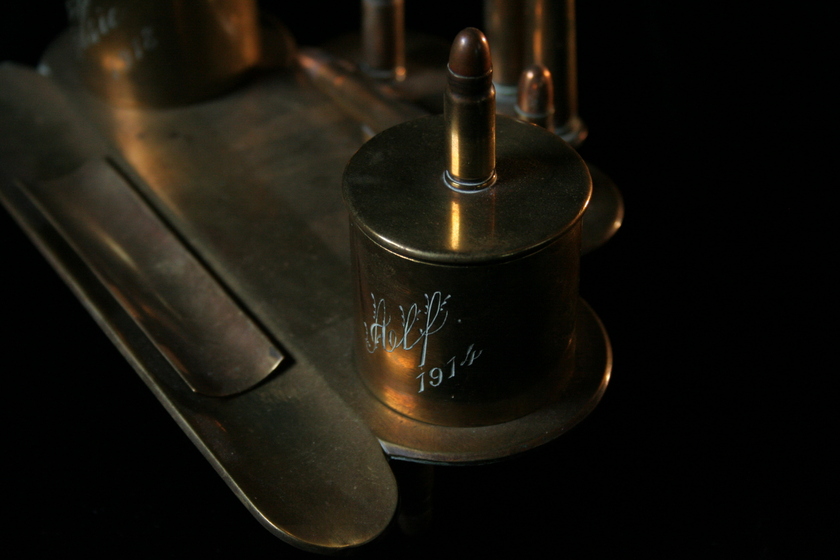 Brass item made from a flat base and attached bullets and casings, with engraved text on the casings. 