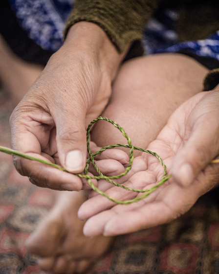 Close up of two hands holding a coiled piece of twine made from plant fibres.